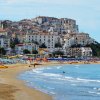 Spiaggia affollata con case bianche in collina.